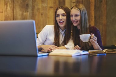 Uzay coworking oturan sınava hazırlık sırasında lezzetli kahve tadını çıkarırken modern Dizüstü aygıtı komik video izleme arkadaşlarım gülümseyerek. Kopyalama alanı alanı reklam metin iletinizi için