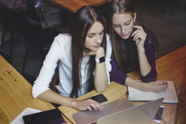 Güzel hipster kızlar macbook bilgisayar kablosuz 4 g için bağlanma hakkında bilgi ararken Internet Web tarama. Dalgın Gençler okul sırası vasıl coworking cihazda modern dizüstü oturuyor