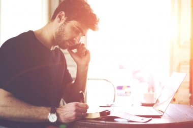 Telefon yoluyla iletişim ve dizüstü bilgisayar kahvehane iç oturan Not Defteri metin bilgileri yazma erkek öğrenci. Sakallı erkek cep üzerinden mobil sohbet
