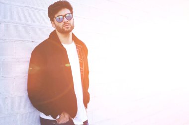 Yarım uzunluk portre emin yakışıklı şık güneş gözlüğü kentsel ayarı yeniden oluştururken kameraya bakıyor. Genç adam metin reklam için kopya alanı ile duvara ayakta sakallı