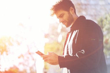 Takipçileri ile haber paylaşımı ve yürürken kişisel web sitesinde modern telefon mesajları gönderme düşünceli yakışıklı erkek blogger. İyi görünümlü genç adam Sokağı'nda modern cihaz ile dinlenme