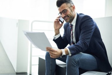 Gülümseyen yakışıklı erkek girişimci başarılı iş planı smartphone, iyi çalışma teklif alma telefonda konuşurken müreffeh olgun yönetmen ile iletişim sırasında rapor okuma memnun