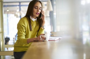 Modern kafede oturan telefon görüşme yoluyla rezervasyon yapma dalgın profesyonel Yöneticisi şık aşınmaya mobil telefon üzerinde proje fikirleri tartışmak iş kadını konsantre