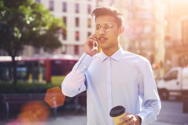 Kendine güvenen genç turist güneş caddeleri civarında geziniyor ve kablosuz internet'e bağlı cep telefonu konuşurken trendy kıyafeti giymiş. Street serbest zaman harcama gözlük iyi görünümlü adam