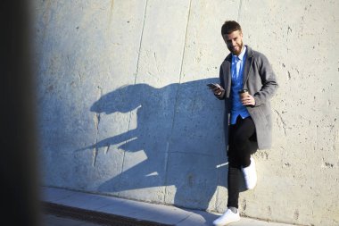 Internet kullanıcı için fotoğraf makinesi ile cep telefonu ve kahve duran arka plan kopya alanı için promosyon içeriği ile kentsel bir ortamda yürüyüş sırasında poz gülümseyen tam uzunlukta portresi