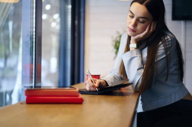 Düşünceli çekici öğrenci el kafede oturan ve ağaç vaktinizi defter şiirlerinde aşağı yazma kalemi ile. Metin bilgileri Not Defteri'nde belirterek ve ödev rüya gibi hippi kız