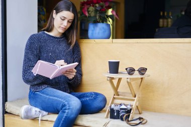 Not Defteri'nde yazma kafede oturan hobi serbest zaman harcama dalgın genç esmer kız. Kadın gezgin kahve terasta otururken notlar yolculuk yapma konsantre 