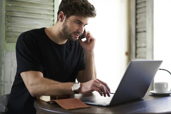 Schöner Junger Mann Der Freundlich Telefoniert Während Ferngesteuert Laptop Arbeitet — Stockfoto