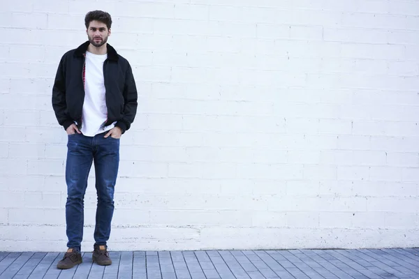 Full length portrait of stylish hipster guy standing on white promotional background for your advertising text message.Handsome man dressed in casual outfit looking at camera near copy space area