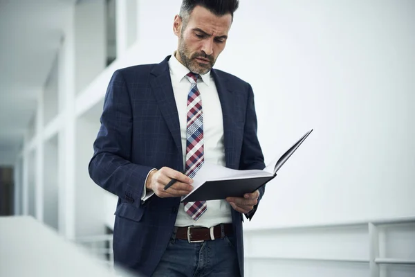Confident male entrepreneur in formal outfit proofreading financial report checking incomes of trading corporation standing near copy space for advertising, pensive executive analyzing documentation