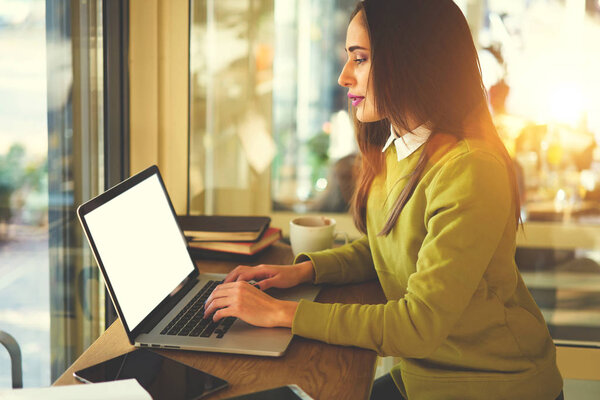 Confident businesswoman working using technology searching information in networks, brunette female entrepreneur using application for making online report via laptop computer with mock up screen