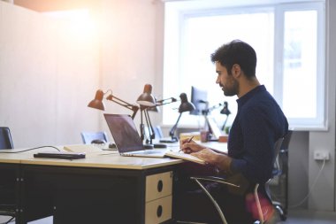 Casual giyim izlerken eğitim webinar üstünde laptop kablosuz internet'e bağlı ve ofis ahşap masada otururken Not Defteri'nde genel fikirler kayıt sakallı yakışıklı çalışan giymiş