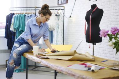 Yetenekli kadın modacı grafik planı örnekleri için yaratıcı fikirler aletleri modern showroom Studio'yu kullanarak çizimler üzerinde gözlük yetenekli terzi olan çizim trendy kot giymiş