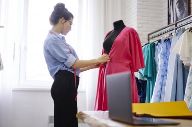 Profesyonel şık giyimli modacı yetenekli kadın atelier trendy elbise model oluşturma sırasında aletler kullanarak topluluğu hakkında düşünme yeni örnekleri üzerinde çalışan manken elbise ölçümü yapma