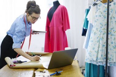 Showroom, çekici yetenekli tasarımcı blueprint modern stüdyo atelier terzilik oluşturmaya konsantre kağıt üzerine çizim çizimler modeli için dizüstü bilgisayar kullanarak dalgın esmer modacı 
