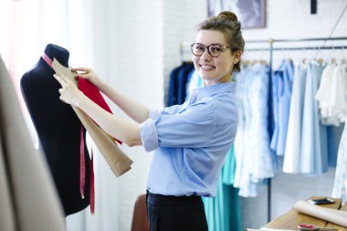 Yarım uzunluk portre neşeli muhteşem atelier sahibinin manken Studio'yu kullanarak malzeme ölçme yaparken kameraya bakıyor. Çekici kadın Tasarımcısı içinde iş elbisesi ile gözlük gülümseyen