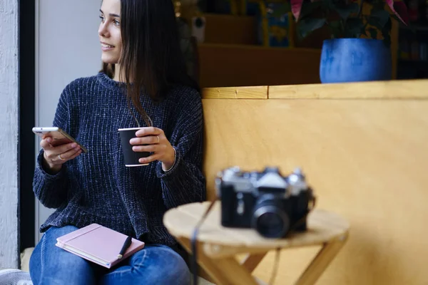 カフェのテラスに座って自由な時間とコーヒーを楽しむカジュアルな服装で笑顔の若い女性 魅力的な女性旅行者のローミングと現代のスマート フォンのインターネットを使用して通信 — ストック写真