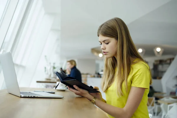 聪明的时髦女孩阅读课本坐在数字电脑设备在 Coworking 聪明的女学生手里拿着笔记本 在室内的咖啡馆里搜索信息 复制空间区域 — 图库照片