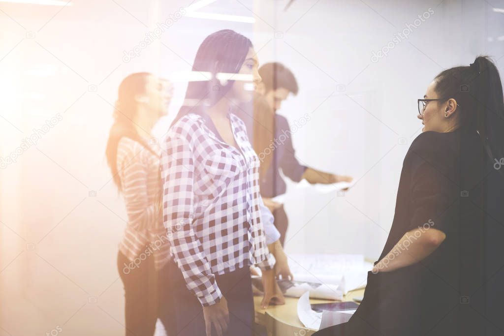 Skilled young afro american employees dressed in casual outfit communicating with experienced manager and discussing working process while colleagues on background collaborating on startup project