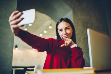 Genç esmer kadın serbest çalışma sırasında kız öğrenci eğleniyor molası smartphone kamera selfie yapmak için poz alarak görüntü üstünde hareket eden telefon Üniversitesi Kampüs witn netbook içinde oturan