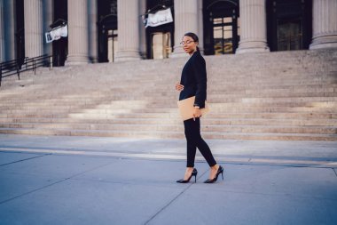 Afro-Amerikan işkadını umut verici kariyer ile tam uzunlukta portresi adliye binası yakınındaki yürürken kameraya bakarak şık takım elbise giymiş. Kopyalama alanı alanı finansal bilgi için