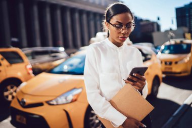 Güzel Afro-Amerikan işkadını Navigator'da modern cep telefonu üzerinden online sarı taksi izleme beyaz gömlek giymiş. Genç erkek şehir şehir merkezinde yürüyüş taksi uygulaması kullanarak