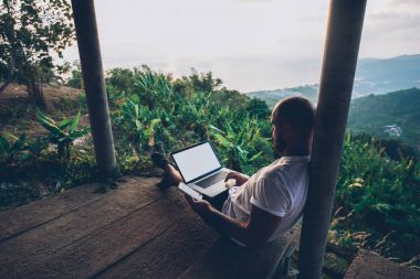 Güzel tabiat Amazon nehri manzarası Uzaktan çalışırken karşı dizüstü bilgisayar ile serbest üzerinde oturan genç adam. Adam Gezgin internet kullanarak doğa görünümü otururken Smartphone'da bankacılık