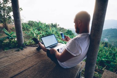 Uzaktan serbest hareket eden zevk üzerinde çalışırken dizüstü bilgisayar ve smartphone kullanarak genç hipster adam Gezgin görünümünü geri. Usb ağ modem aygıtı ile internet'e bağlanan cihazların erkek