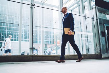 Yakışıklı genç erkek girişimci cam cephe ile takım geçen modern ofis bina, kurumsal takım ile klasör Manhattan'ın şehir merkezinde yürüyüş emin iş adamı tam uzunlukta görünümünü