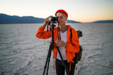 Genç kadının iş doğal Doğa ortamında modern donanımları, profesyonel kadın fotoğrafçı peyzaj Badwater Havzası tripo ile fotoğraf makinesinde video çekim fotoğraf yapma