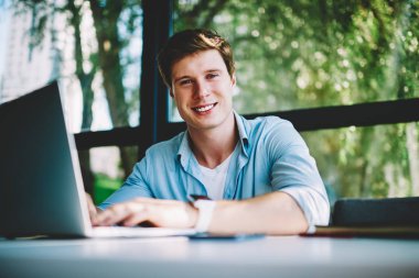 Modern laptop, başarılı genç işadamı serbest zevk ücretsiz programa kameraya bakarak online para kazanmak yeni yazılım güncelleştirme ile neşeli erkek programcı portresi memnun