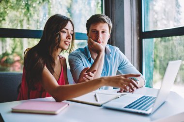 Proje web sayfasında, bilgileri kullanarak çevrimiçi alışveriş yapma arkadaşlarım işaret eden kadın meslektaşı ile işbirliği üzerinde çalışma düşünceli erkek öğrenci portresi dizüstü bilgisayar kafe iç