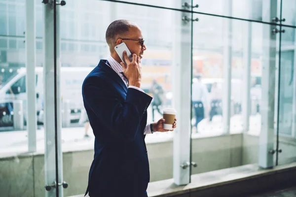 Confident man proud CEO in formal wear having mobile phone conversation about business during coffee break, skilled male entrepreneur lawyer talking on smartphone standing outdoors in city downtown