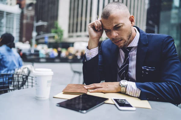 Worried man entrepreneur angry about problems with financial report while checking numbers in report, irritated businessman getting bad news checking email via touchpad while sitting on downtown cafe