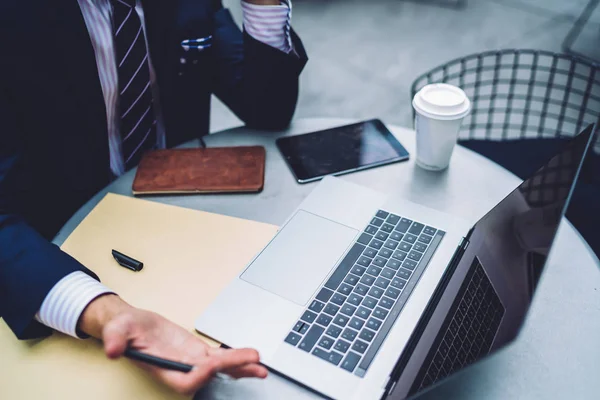 Cropped image of proud CEO in suit working on project sitting with laptop computer at table, close up view businessman making researches gesturing while angry about software failure on netbook