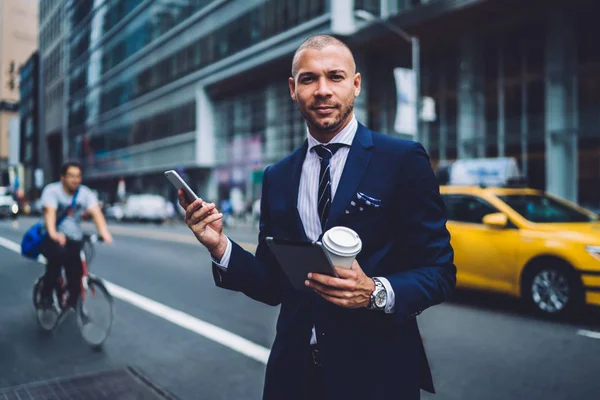 Half-length portrait of prosperous executive manager making call to taxi service getting to office with gadgets, handsome businessman using devices for browsing information walking outdoors