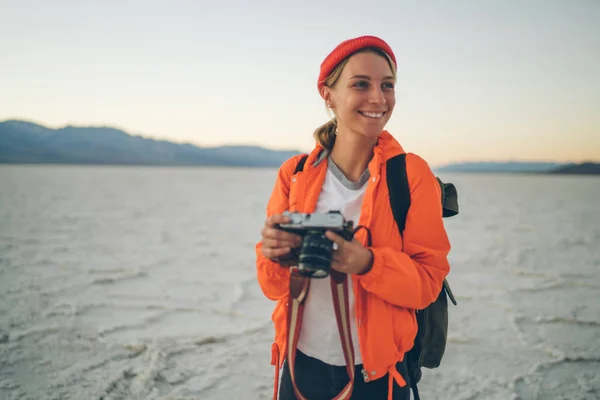 Smiling tourist woman holding camera while enjoying nature view having expedition in Death Valley during travel in USA, positive female blogger happy exploring Badwater basin with her digital camera