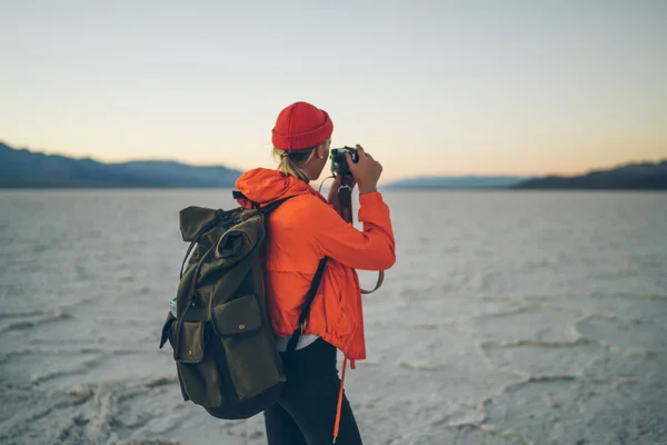 Back view of female photographer taking picture of natural landscape of Badwater basin, woman using professional camera making image exploring unique environment of Death valley national park in US