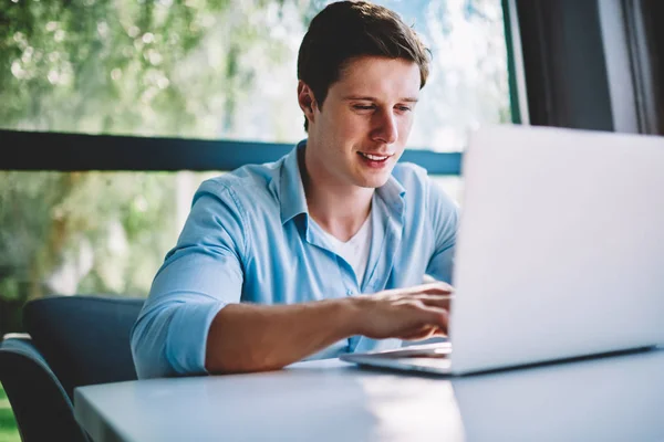 Skilled hipster guy concentrated on information during e-learning courses typing on laptop computer, young male freelancer satisfied with remote job creating publication for websites keyboarding
