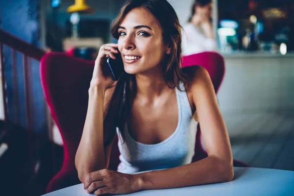 Young woman in casual wear having phone conversation with friend during free time in cafe interior, pretty hipster girl having phone consultancy with operator about tariffs for mobile calls