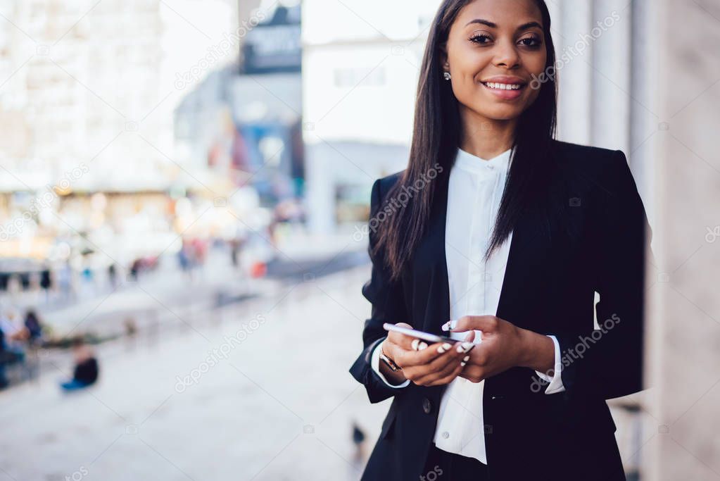 Cropped portrait of charming African American economist in formal elegant wear making money payment on website  via smartphone smiling for the camera. Successful businesswoman posing with cellphone