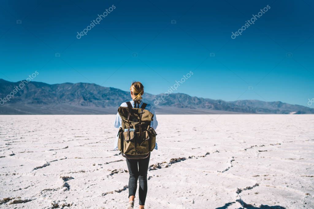 Back view of female traveler exploring death valley national park carrying equipment in rucksack for taking photo,young woman walking on touristic route in beautiful natural landscape on daytim