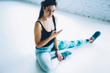 Mobil bloglama sosyal ağlar, smartphone cep telefonu ile spor salonunda egzersiz oturum ileti gönderme sırasında dinlenme kamera seyir genç fitness kız için kullanarak bacak germe sporcumuz portresi