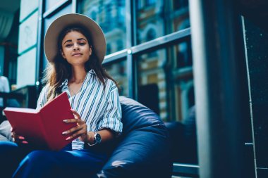 Başarılı öğrencinin yarım uzunluk portre ünlü yazar alanı coworking içinde serbest zaman sırasında kopyalama alanı alanı yakınındaki yumuşak kabarık üzerinde dinlenme yeni kitap okuma zevk şık casual giyim giyinmiş