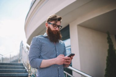 Optik Gözlük online sosyal ağlar üzerinde modern telefon kentsel ortamda yürürken Ücretsiz 4 g internet bağlantısı kullanarak sohbet akıllı sakallı öğrenci. Metin için promosyon arka plan