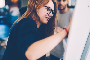 Dikkatli bir şekilde iş başlangıç projesi alan coworking içinde ayakta için genel kavramları aşağı yazma genç pozitif kadın işçi. Flipboard üzerinde beyin fırtınası gözlük güzel kadın işveren