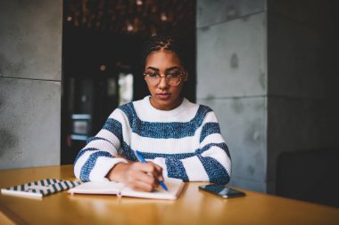 Afro Amerikan öğrenci optik gözlük içeride kahve dükkanında oturmuş ödevlerini yaparken yoğunlaştı. Kafeterya iç eğitim ve sınavları için hazırlık Eyewear dalgın siyah modeli