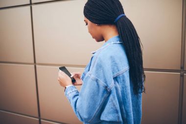 Aranan telefon numarası telefon promosyon arka plan ayakta tarihinde pigtails ile arkadan görünüşü afro Amerikan şık genç kadın. Casual giyinen hippi kız cep üzerinde uygulama güncelleştiriliyor