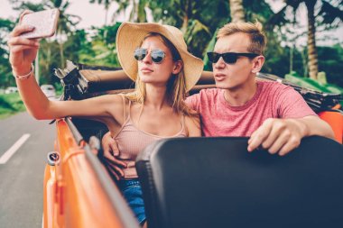 Hippi kız erkek arkadaşıyla ağlarında çift aşk cep telefonunda ortak resim için poz yolculuk sırasında Kiralık Araba üzerinde taşıma, paylaşım için smartphone kamera çekimi selfie kullanarak güneş gözlüğü