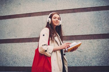 Yarım uzunluk portre çekici hippi kız hippi kız açık havada tutan kitap ücretsiz vaktinizi kulaklık, müzik dinlemek, reklam için kırmızı alışveriş çantası kopya alanı ile gezinme